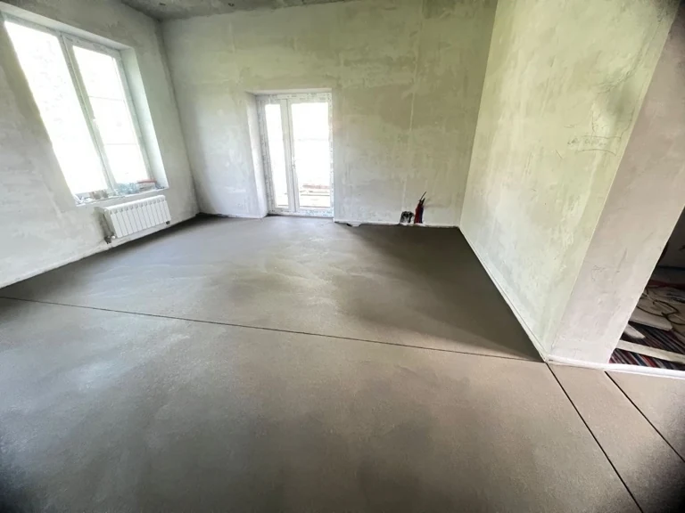 Полусухая стяжка пола 130 м² в частном доме на Речной улице в поселке Старотеряево, Рузский округ - ровная поверхность в комнате с балконной дверью и радиатором