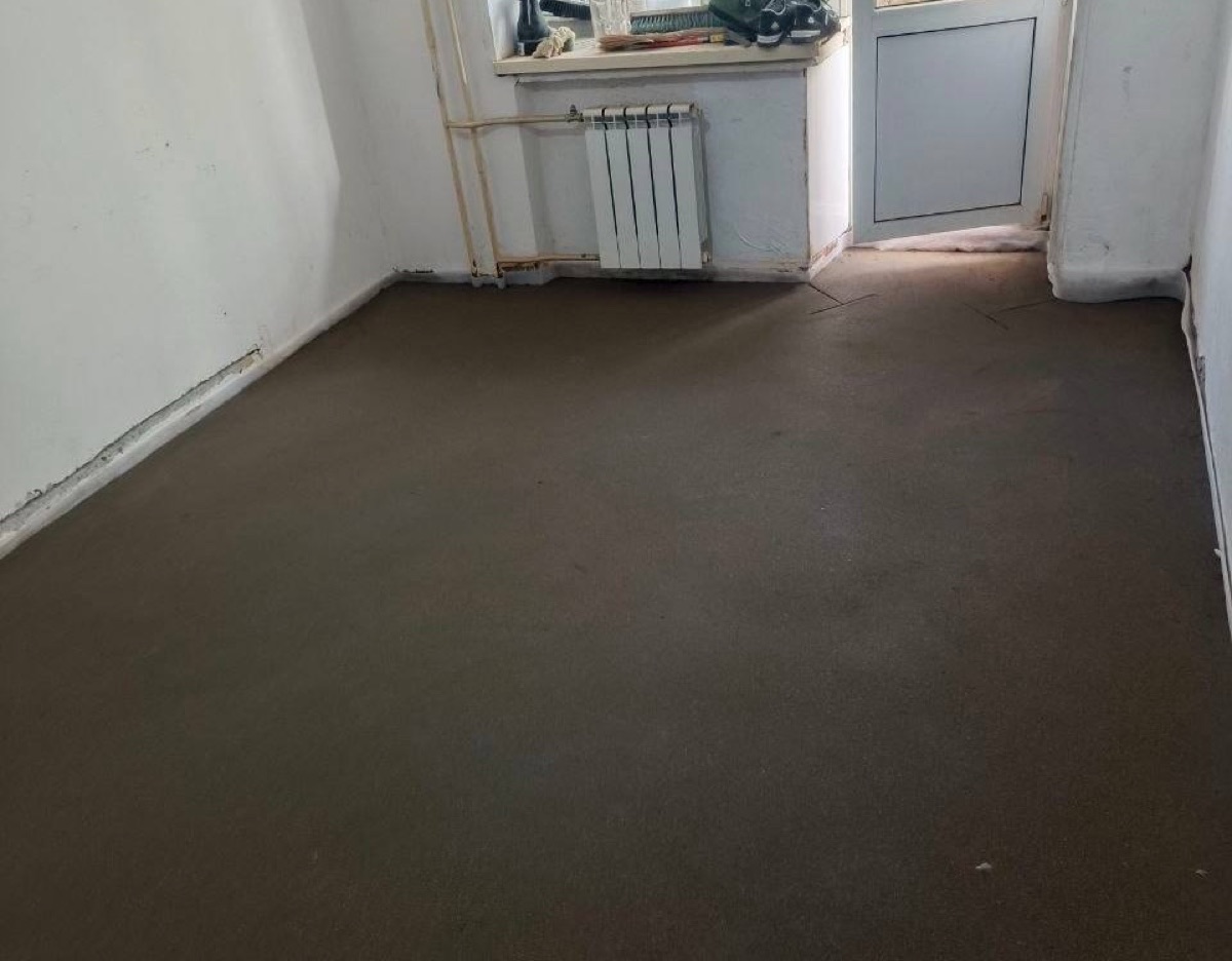 Полусухая стяжка пола 45 м² в квартире на Байкальской улице в Москве — ровная поверхность в комнате с радиатором под окном