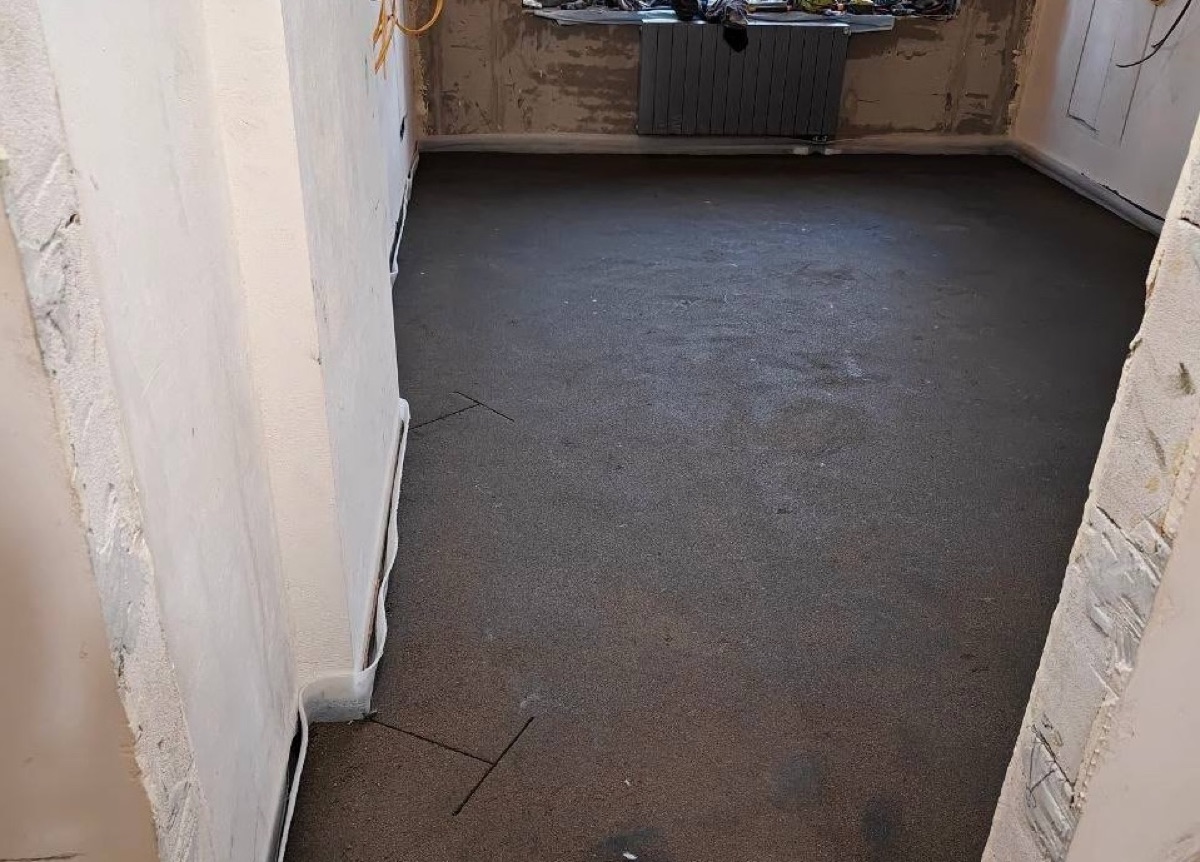 Свежая полусухая стяжка в комнате квартиры 102,6 м² на Клинской улице в Москве — ровный слой у радиатора под окном