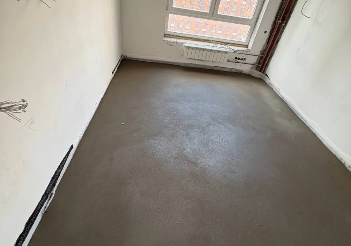 Полусухая стяжка в квартире 85 м² на улице Поляны - комната с окном, радиатором и ровным основанием